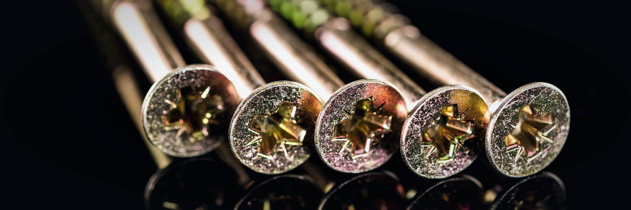Macro photo of yellow zinc-plated screw heads on a black background